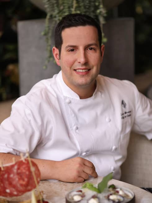 Portrait photo of Chef de Cuisine Luca Moriconi wearing white uniform at table