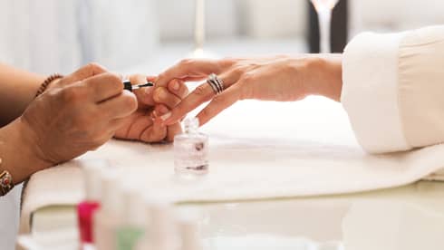 Close-up of woman in white robe getting clear polish manicure at spa table