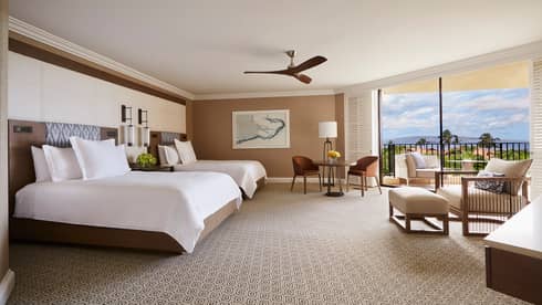 Luxury hotel room with two queen beds, sitting area and large balcony overlooking tropical scenery and ocean 