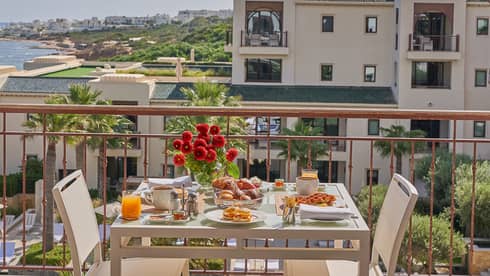 Outdoor table with flowers and elaborate breakfast spread on a balcony overlooking Tunis and water