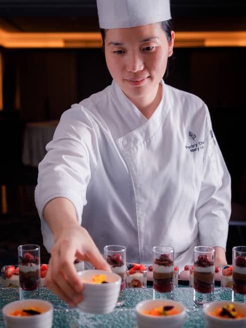 Woman wearing white chef's coat and hat prepares chocolate dessert shooters