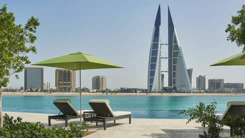 Two lounge chairs under lime-green umbrella on deck looking out at Arabian Gulf, modern tower