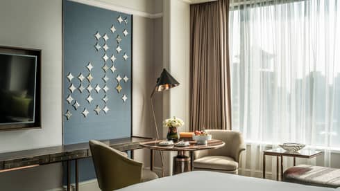 Corner of end of bed, modern chairs around cafe-style table with lamp, Peranakan tiles on wall