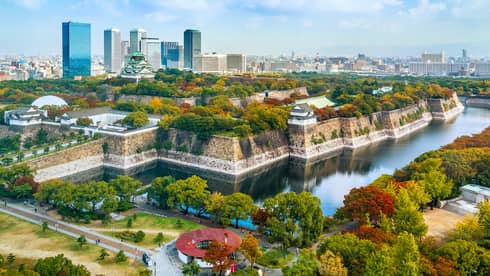 Osaka Castle rises amid lush autumn-coloured trees within a stone fortress surrounded by a moat and modern high-rises.