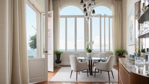 Elegant dining room, table with four chairs, tall windows with sea view