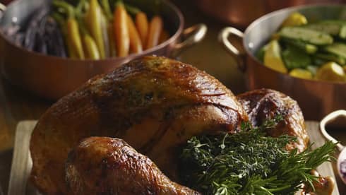 Festive turkey stuffed with rosemary on carving board, accompaniments and side dishes in the background
