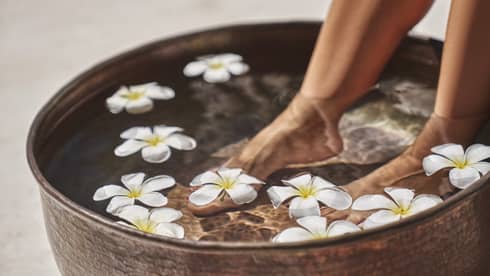 A woman's feet in a bowl of water and flowers.