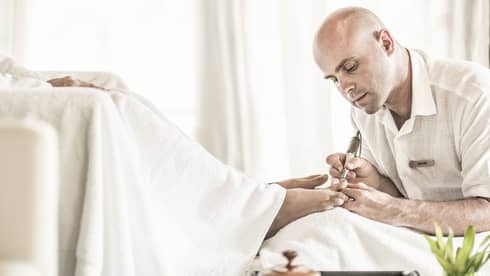 Man holds small pedicure tool at woman's feet in spa