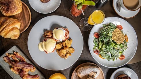 An elaborate brunch, including eggs Benedict, potatoes, bacon, various pastries, salad, a bloody mary and mimosas