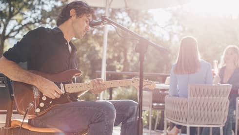 Man plays electric guitar at microphone on sunny patio