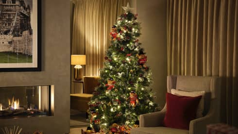 Christmas tree lit up in a dimly lit living room with fireplace