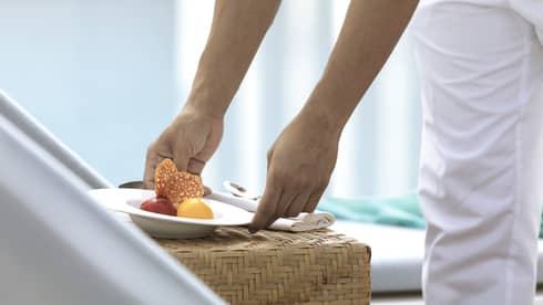 Close-up of hands placing white bowl with scoops of sorbet on wicker table