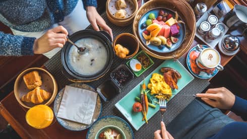 View from above as two guests savour a sumptuous array of vibrant dishes, including pastries, congee, fresh fruit and coffee.