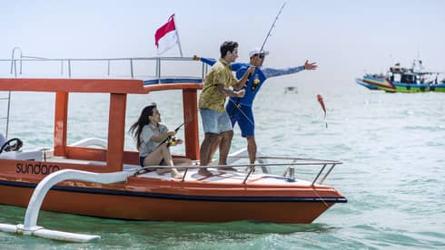 Tour guide teaches two guests to fish on a traditional jukung fishing boat on the open ocean