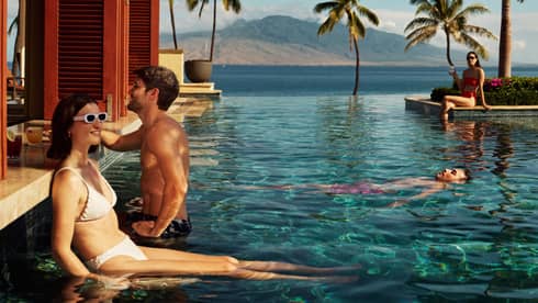 Guests enjoying an infinity pool with ocean and mountain views, surrounded by palm trees at a luxury resort