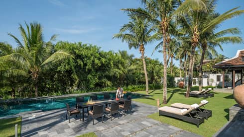 Server sets long patio dining table by Hilltop Villa outdoor swimming pool