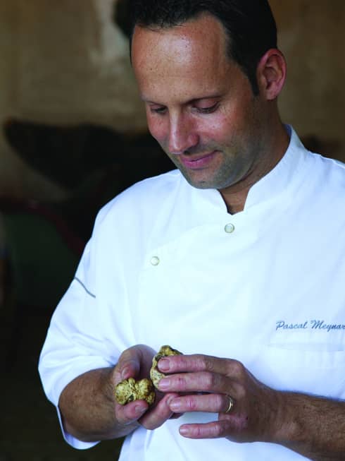 Portrait photo of Executive Chef Pascal Meynard wearing white chef's uniform, looking down at mushrooms in hands