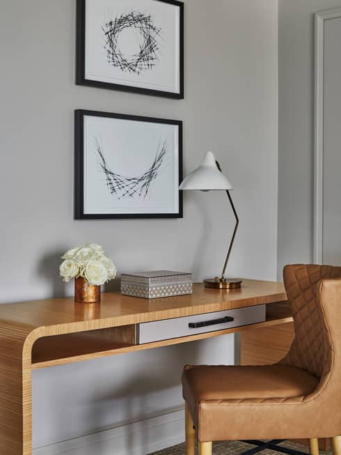 Retro-style leather chair, wood desk with white roses, lamp under framed prints