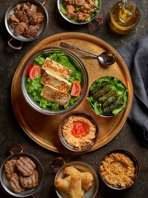 Three strips of fried Halloumi cheese on bed of lettuce in bowl, tomato wedge