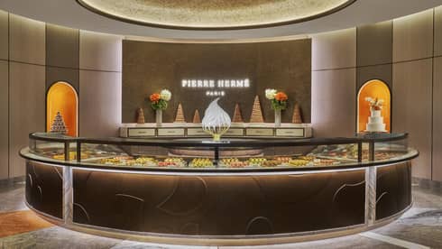 Circular pastry counter with the name Pierre Herm� light up on the wall behind it
