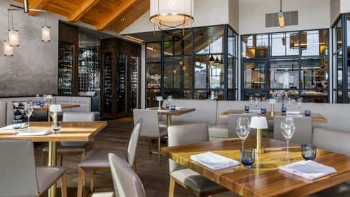 Restaurant with square wooden tables, light grey chairs, and vaulted ceiling