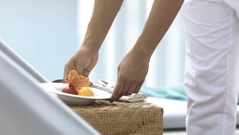 Close-up of hands placing white bowl with scoops of sorbet on wicker table
