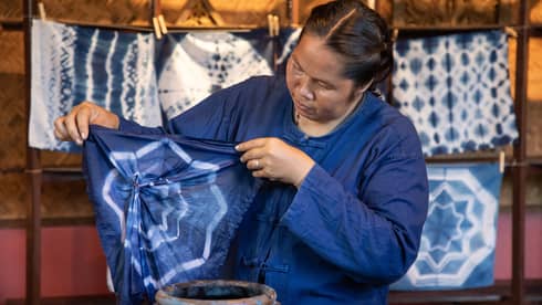 A woman in a blue overshirt, dyeing a piece of fabric.