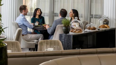 Four guests sitting together at a dining table in a dining room with floor-to-ceiling windows.
