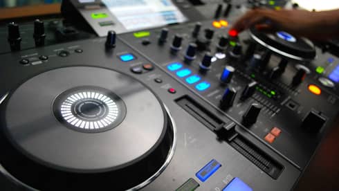 Close-up of DJ console discs, buttons, lights, hand adjusting levels