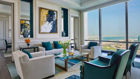Hotel room living area with beige, green and gold seating area, modern art on wall, sunny windows