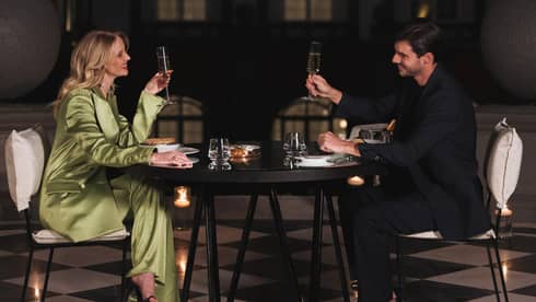 A man and woman drinking in a dimly lit room at a dark table.