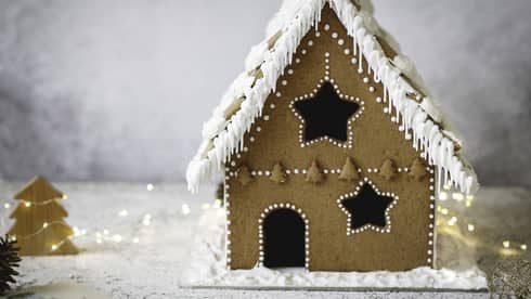 Gingerbread house decorated with white icing amid white background and white lights