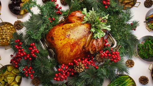 Festive whole turkey with holly berry and pine cone garnish, surrounded by side dishes