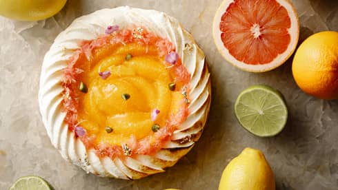 Aerial shot of whole citrus tart rimmed with pastry cream, halved citrus fruit on table surrounding it