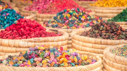 Close-up of multiple round woven baskets bursting with a rainbow of colourful herbs and spices and dried red flowers.