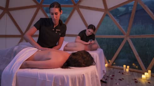 Couple lying on spa tables in yurt, receiving massages from spa therapists