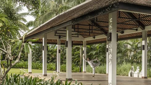 Man does yoga in outdoor yoga pavilion surrounded by palm trees