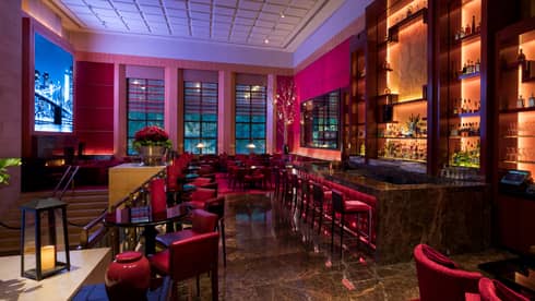 Ty Lounge at dusk with red velvet chairs, stools, lanterns on tables, lights behind bar 