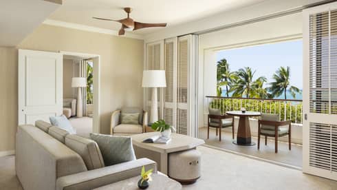 Elegant resort suite living room, featuring a beige sofa facing a furnished balcony with tropical ocean views