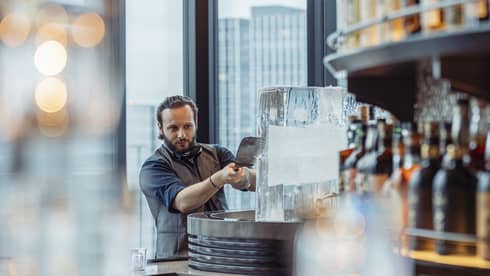 Male bartender shaves ice off a large ice block at luxury hotel bar