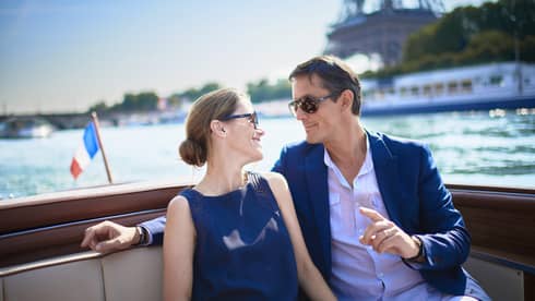 Couple enjoy Paris boat ride next to small France flag, Eiffel tower in background