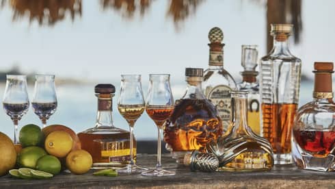 Whisky glasses surrounded by tequila, whisky and rum bottles, with a small pile of lemons and limes off to one side.