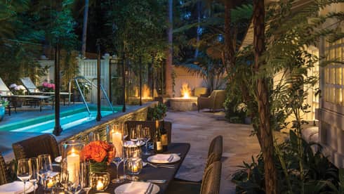 Ty Warner bungalow backyard candle-lit patio dining table by plunge pool, fire pit at night