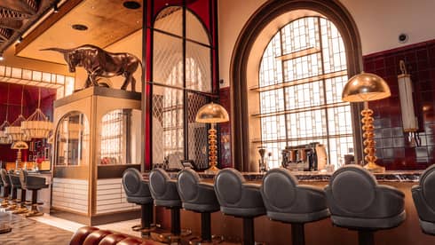 Bar area of a restaurant featuring blue leather bar stools, large brass lighting and 1920s-style decor