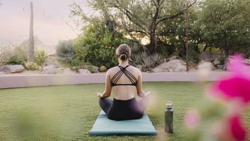 Person doing yoga outside on a blue yoga mat with a water bottle beside them.