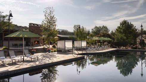 An outdoor pool with lounge chairs and green umbrellas near it.