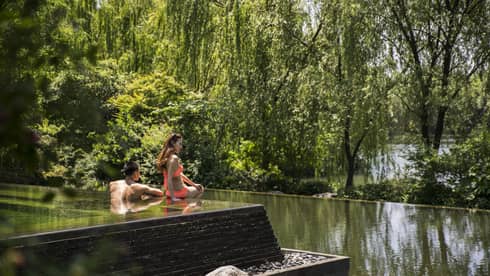 Woman in orange bikini sits on edge of swimming pool in front of man