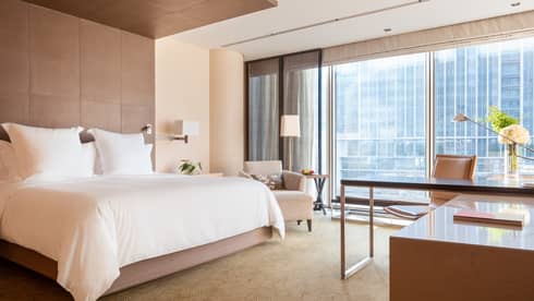 Guest room with large windows, city views, king bed, lamp, armchair and workspace