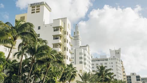 Art Deco buildings with palm trees in front under a bright, partly cloudy sky.