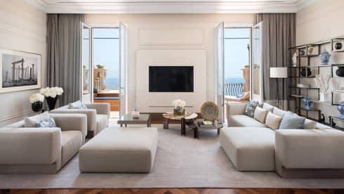 Living room with contemporary grey sofa, two matching arm chairs and large ottoman, TV on wall, two doors leading to balcony